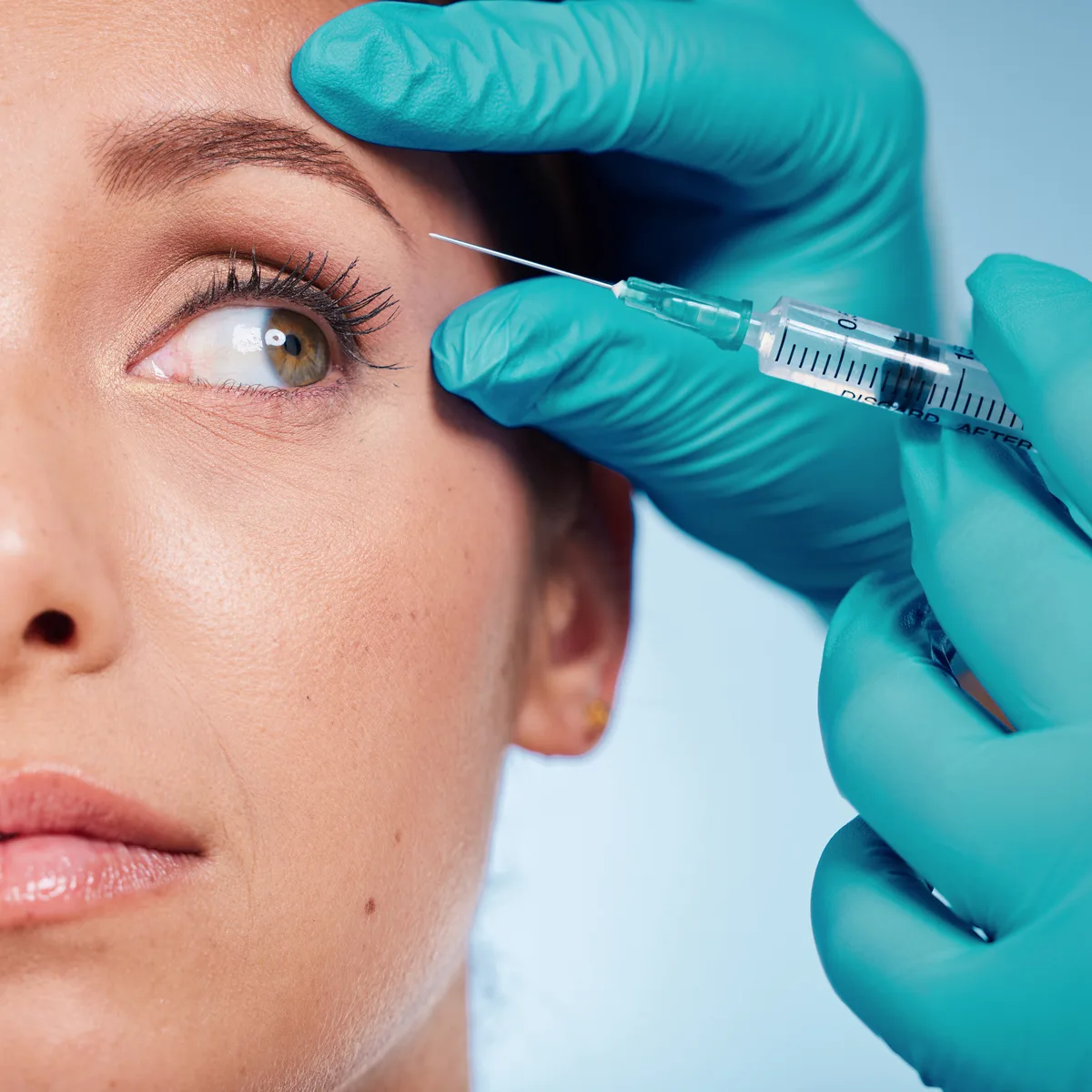 Close-up of a woman receiving an injectable treatment near the brow from gloved hands at Kenzi MedSpa in Naples